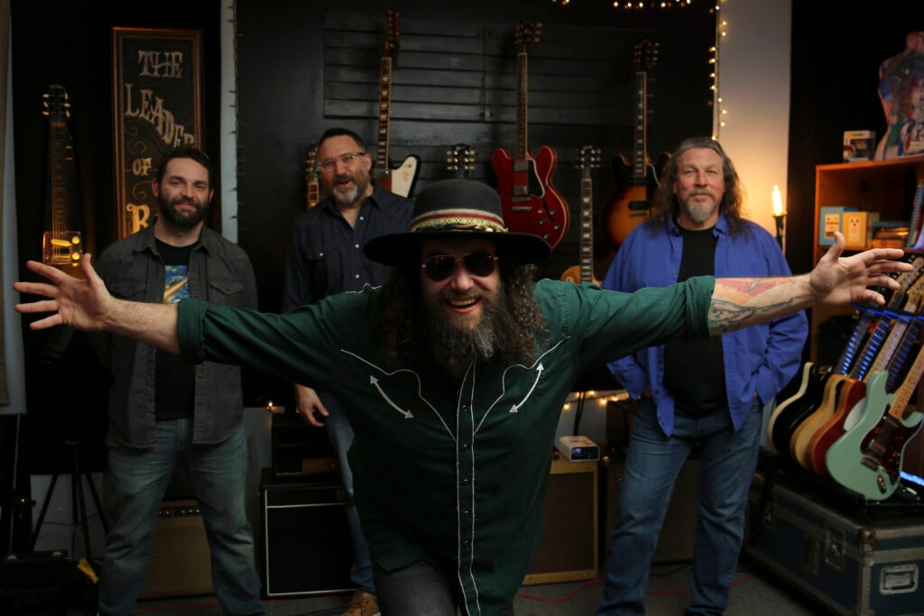 Nate Gross Band press photo: guitarist in wide-brim hat arms outstretched in guitar studio