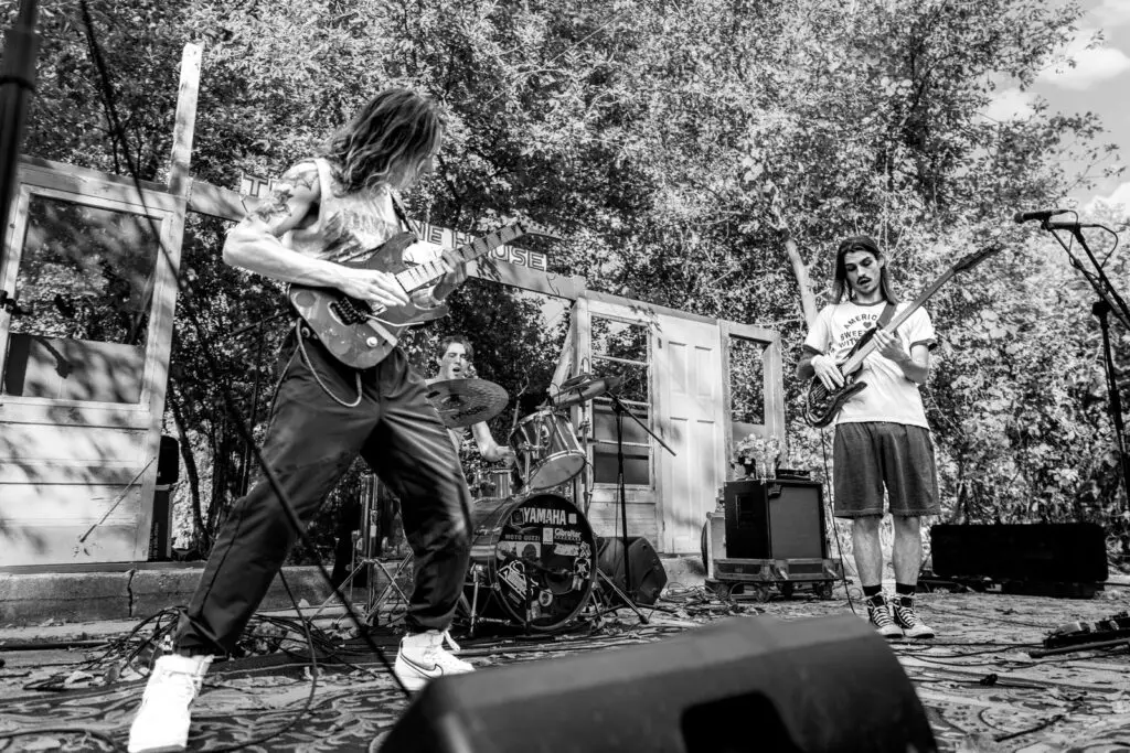 Flagman performing live on outdoor stage, three-piece alternative metal band, black and white