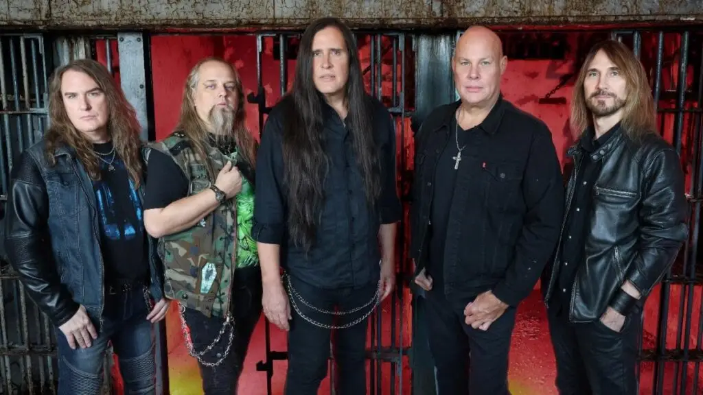 Metal Church band press photo 2026 – five members in leather posed in front of iron bars with red lighting