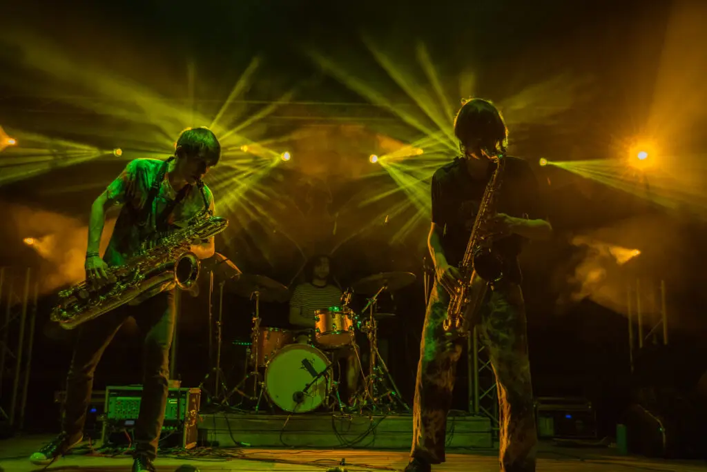 Big Blitz performing live — two saxophonists and drummer under dramatic green and gold stage lights