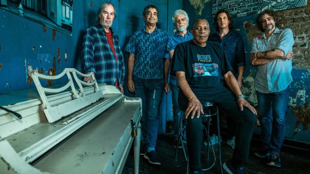 Little Feat band members pose in a weathered blue room with an old upright piano
