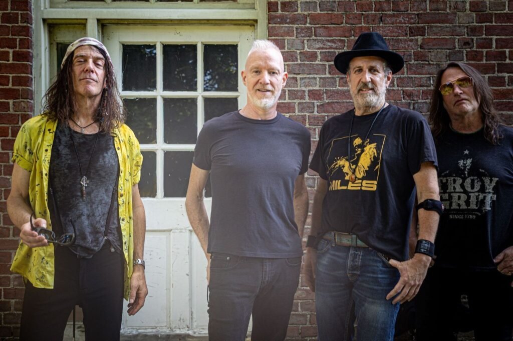 Spin Doctors pose for 2027 tour announcement photo in front of a brick building