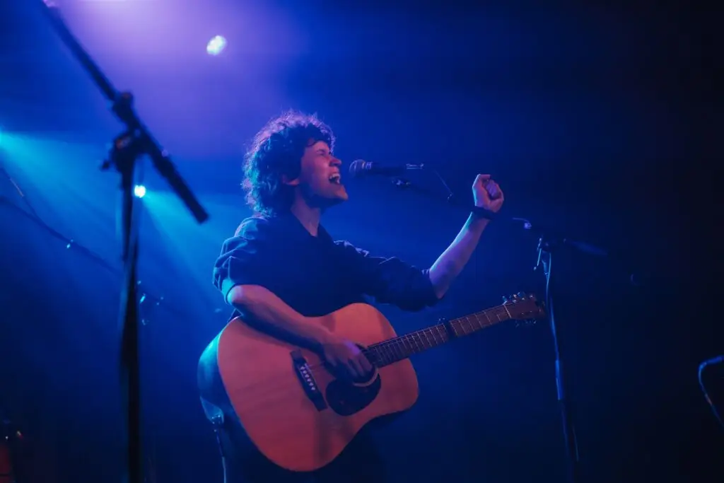Spencer LaJoye performing live at a concert, singing at microphone with acoustic guitar under blue stage lighting
