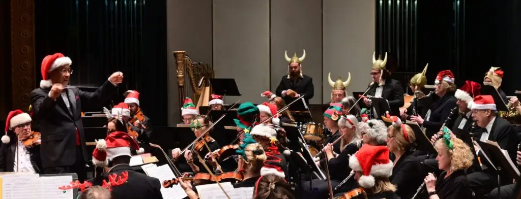 Orchestra of the Southern Finger Lakes holiday concert at Clemens Center, conductor leading full orchestra in festive hats
