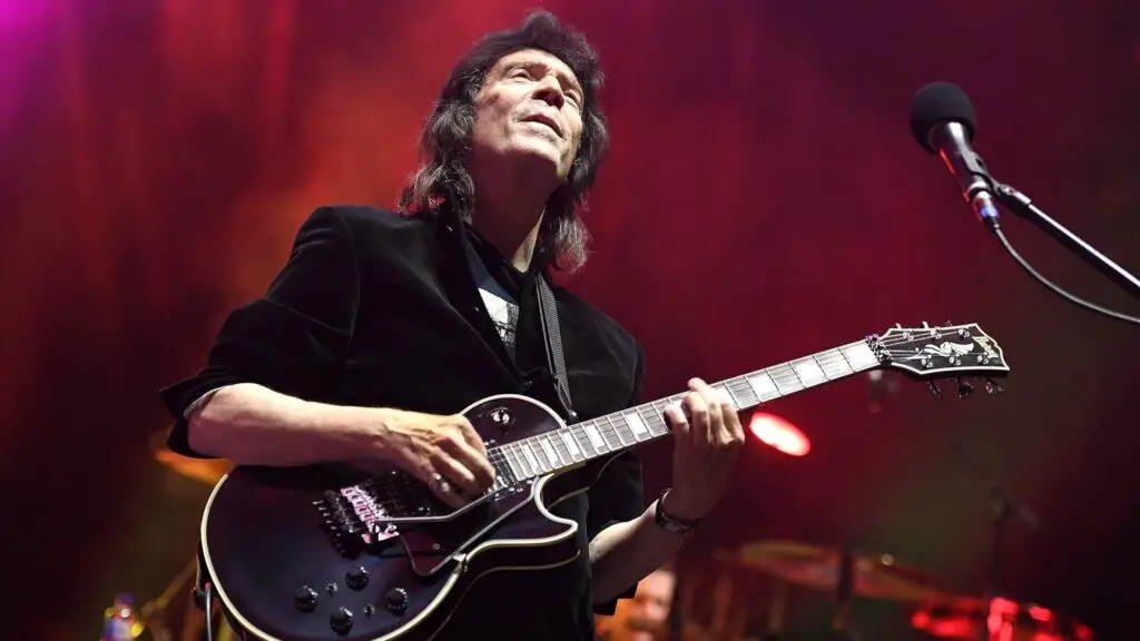 Steve Hackett playing electric guitar on stage with dramatic red lighting during a live concert performance