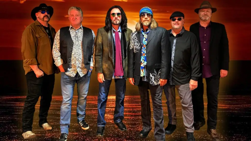 Free Fallin performing the Tom Petty Concert Experience — six-piece band in retro rock attire, dramatic sunset backdrop