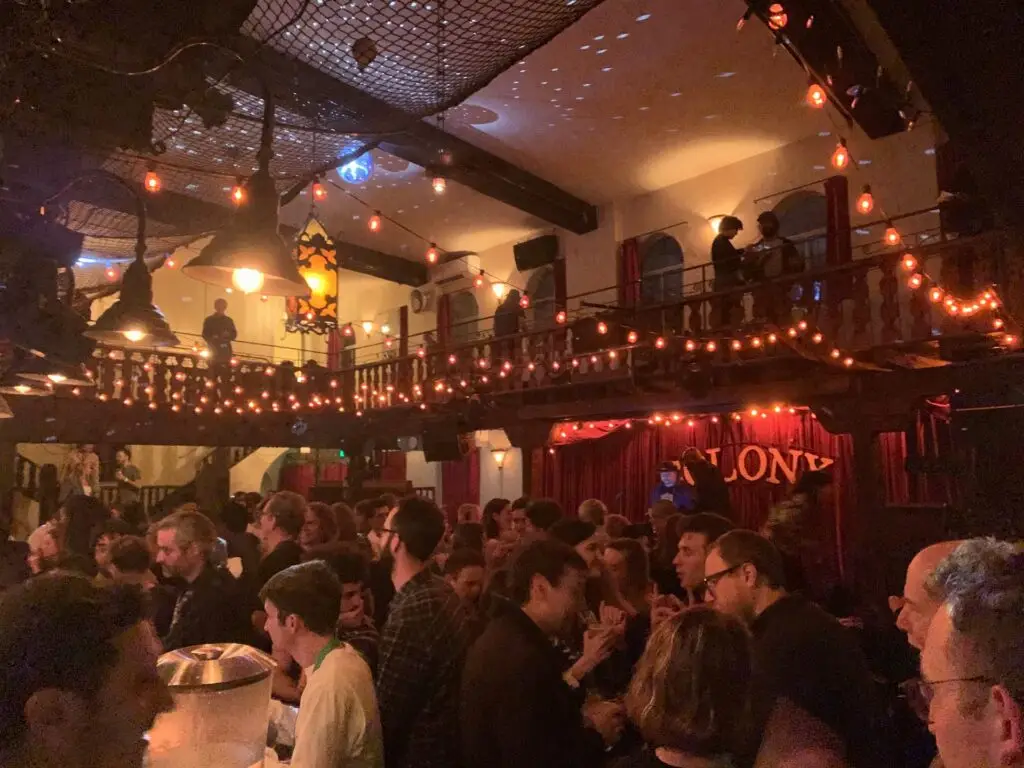 Colony Woodstock great room interior with packed crowd, two-story balcony, string lights, and stage