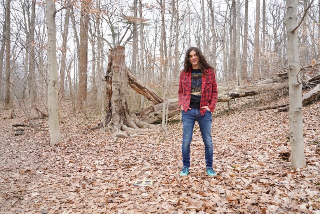 Kurt Vile standing in a woodland outdoor setting, press photo by Adam Wallace-Cavage