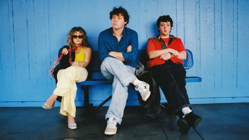 Boys Go To Jupiter trio seated on a blue bench against a blue wall, press photo