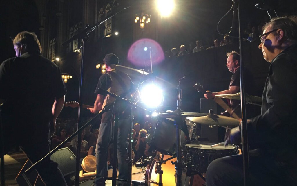The Smithereens performing live on stage, viewed from behind, packed crowd in ornate venue