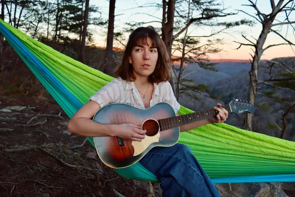 Maya de Vitry playing guitar in a hammock on a mountain ridge at sunset