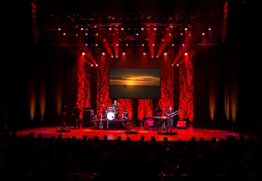 Hotel California — The Original Eagles Tribute performing live on stage with dramatic red lighting in a theater