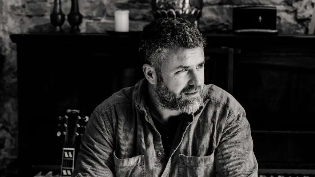 Mick Flannery, Irish singer-songwriter, seated in a rustic stone interior with acoustic guitar