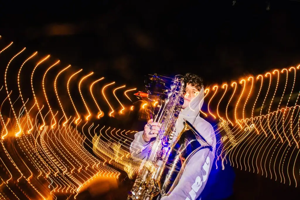 Michael Wilbur playing bass saxophone with sweeping orange light trails in a live performance photo