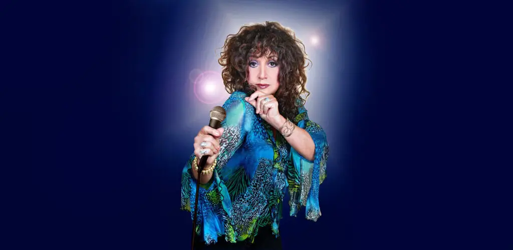 Maria Muldaur holds a microphone in her official press photo