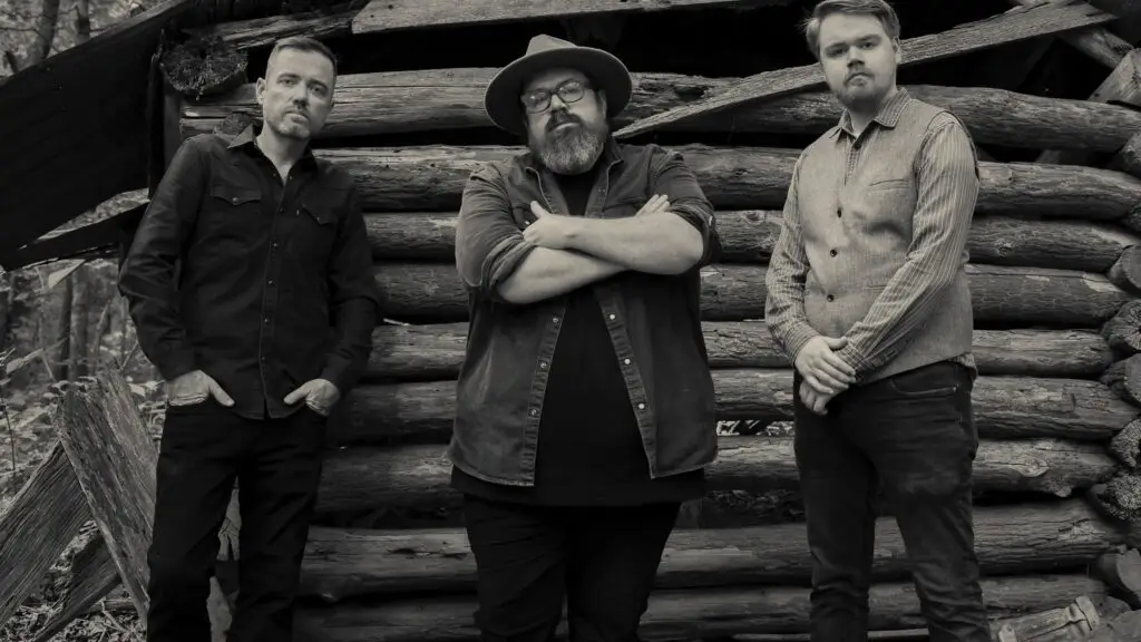 Garrett Boys — trio standing before a rustic log cabin in the woods, official press photo