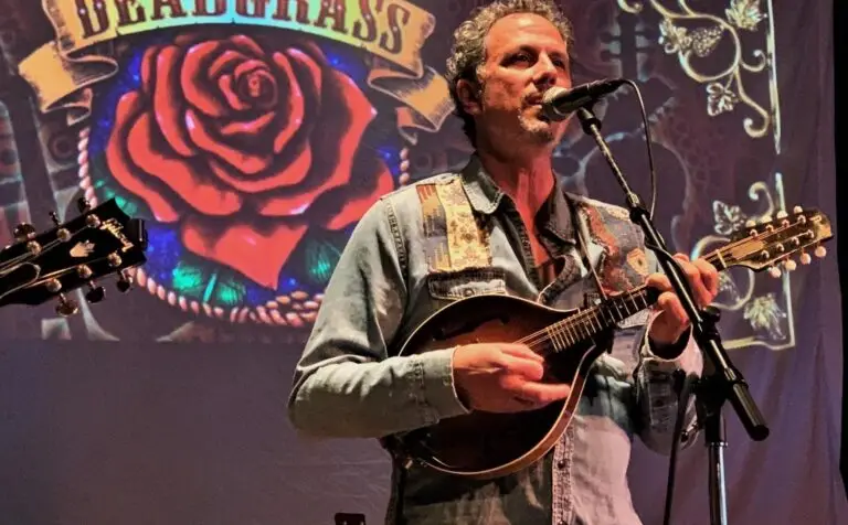 Deadgrass performer playing mandolin at microphone on stage, with Deadgrass rose-banner backdrop