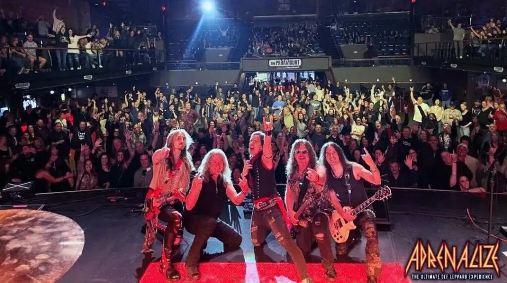 Adrenalize performing live at The Paramount, five members on stage with raised hands before a packed crowd